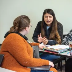 Two students engaged in a lively conversation while sitting at a table.